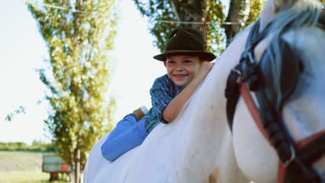 portrait of a little smiling boy with a hat lying on a horse's back and looking at the camera