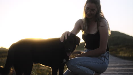 mujer joven interactúa amigablemente con su perro mientras se pone el sol