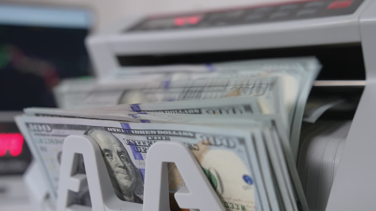 Notes with Benjamin Franklin portraits fall on the holder of cash counting machine. Close up. Blurred background.