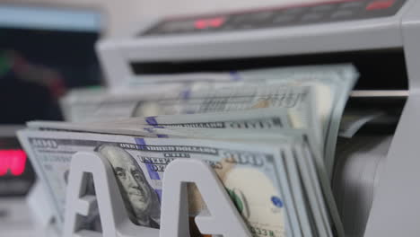 notes with benjamin franklin portraits fall on the holder of cash counting machine. close up. blurred background.