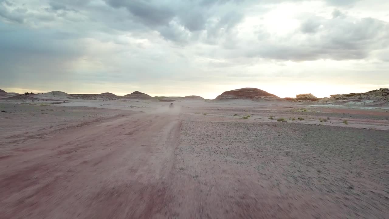 Speedy Tracking Aerial View of Person Driving ATV Vehicle in Dusty Road in Dry Desert Landscape Under Dramatic Sky