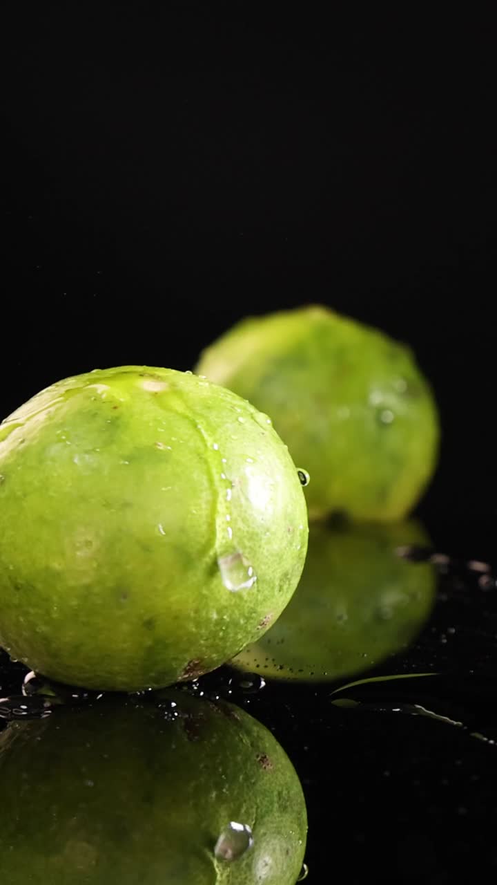 Un limone fresco e verde cade e schizza su una superficie nera lucida al rallentatore