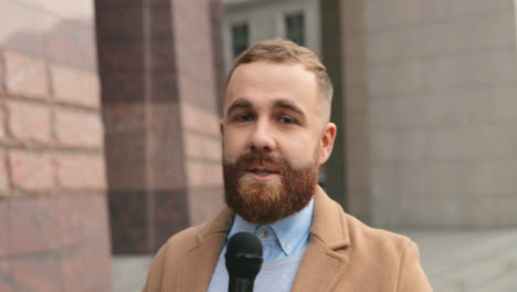 close-up view of smiling caucasian male journalist speaking on the microphone in the street in autumn