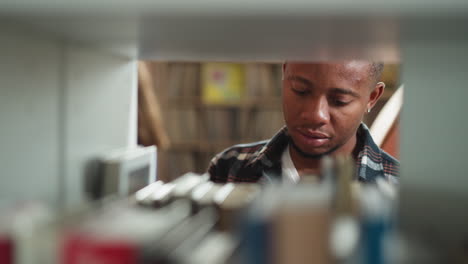 guy looks for book on shelf closeup. focused dark-skinned student seeks literature for essay writing standing in library. searching information for coursework