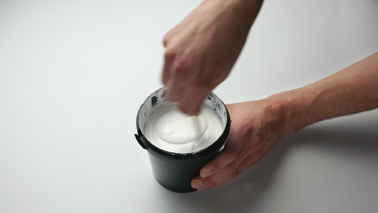 Omrøring af hvid maling i en dåse. Forberedelse til at male væggene. Boligrenovering.