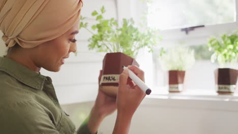 video of biracial woman in hijab writing on herb pots