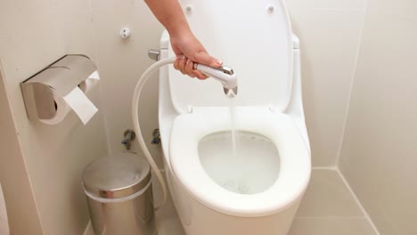 a woman uses a hose to flush water in the toilet to clean