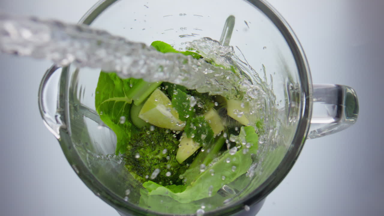 verter agua mezclando verduras en el mezclador de cerca. preparando cócteles de vitaminas