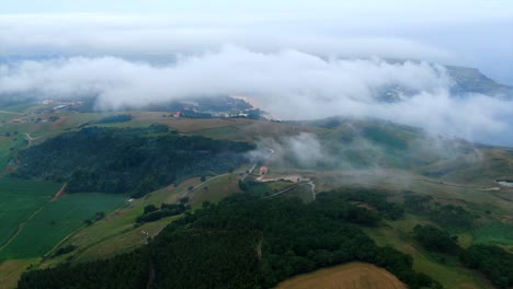 Sie-Fliegen-über-Die-Wolken,-Die-Ein-Einzelnes-Haus-Auf-Einem-Hügel-Umgeben,-Umgeben-Von-üppigen-Grünen-Wiesen-Und-Dem-Meer-In-Der-Ferne