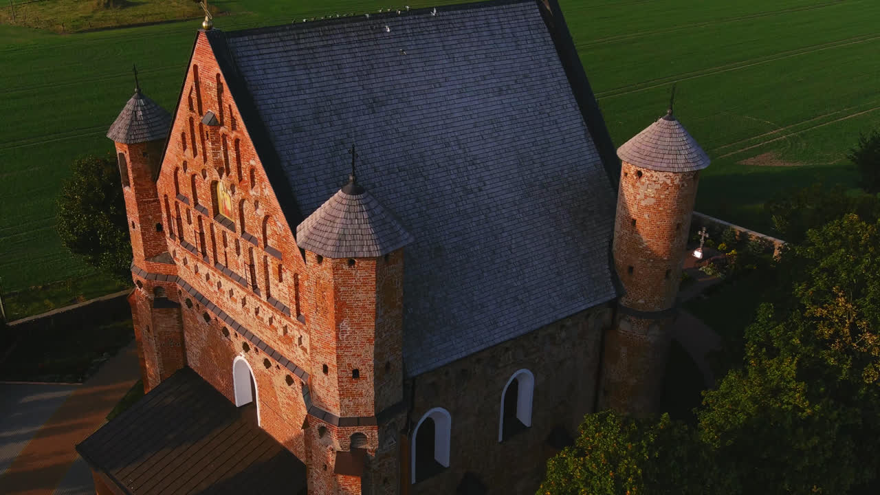 Aufsteigende Drohnenaufnahme einer historischen orthodoxen Backsteinkirche, umgeben von ländlicher Landschaft in Belarus.