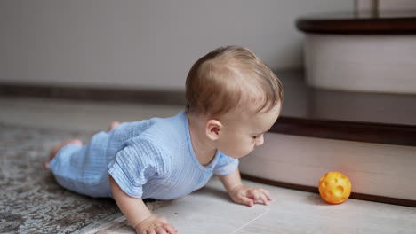 sweet adorable baby boy crawling by the floor indoors. active healthy kid trying to reach a ball. little kid playing with a toy.