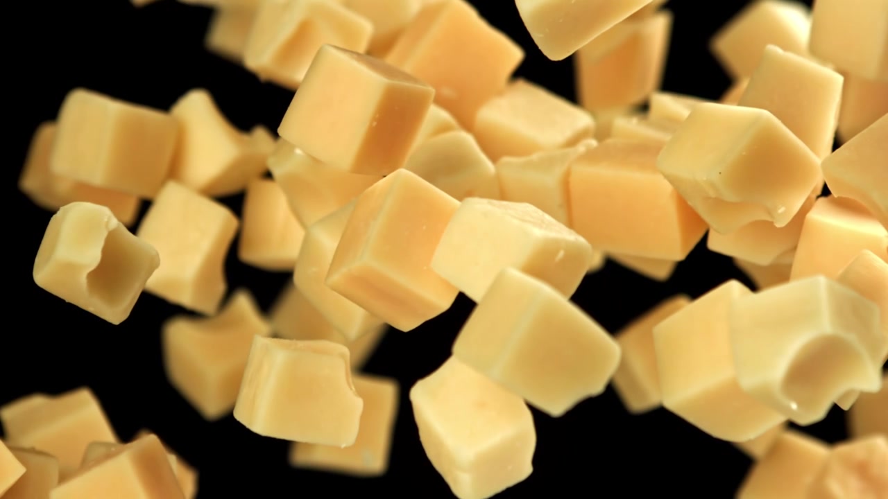 Cubes de fromage tombant au super ralenti sur fond noir.