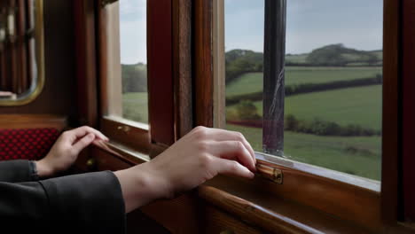 hands resting on a vintage train window with countryside view