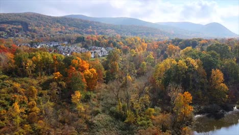 A-drone-shot-paning-sideways-over-a-small-American-town-during-autumn-at-peak-foliage,-with-cloud-covered-mountains-in-the-background-and-some-houses-in-the-foreground