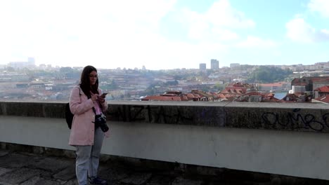 handheld shot of pretty caucasian woman with camera and a phone on rooftop in porto, portugal