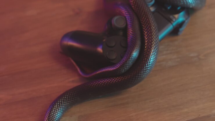 Serpente ratto marrone sdraiato su un controller su un tavolo di legno.