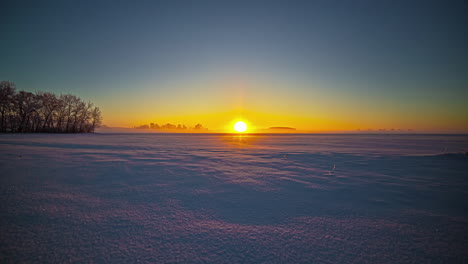 timelapse shot of golden sunset in the background over snow covered agricultural fields during evening time