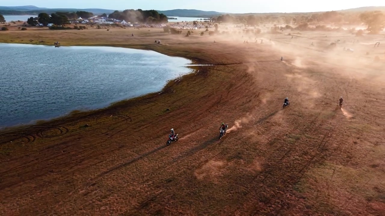 Piloti di motocross che corrono lungo la riva di un lago al tramonto