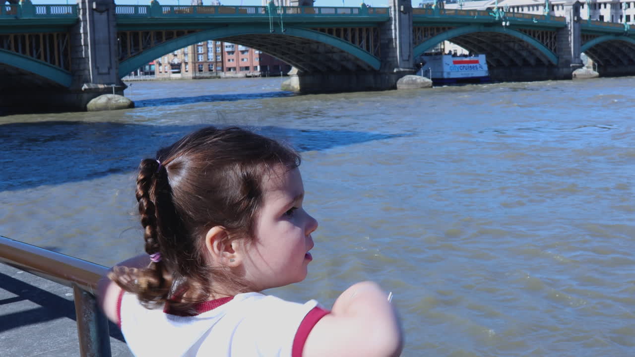A child looks out at the Thames River while waving, with St. Paul's Cathedral visible in the background