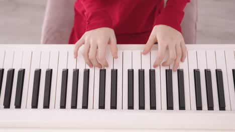 cerca de las teclas de piano blancas y negras siendo tocadas por las manos de un niño pequeño vestido de rojo