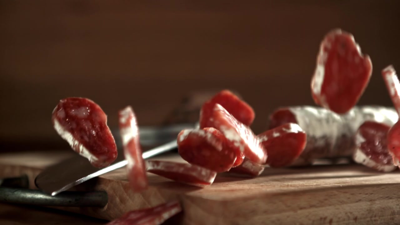 Fette di salame che cadono su un tagliere di legno al rallentatore