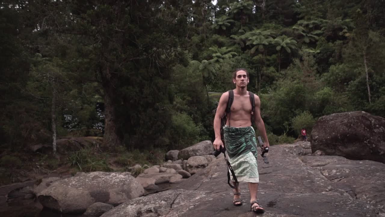 Man walking through a lush forest with rocks and water
