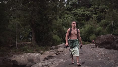 man walking through a lush forest with rocks and water