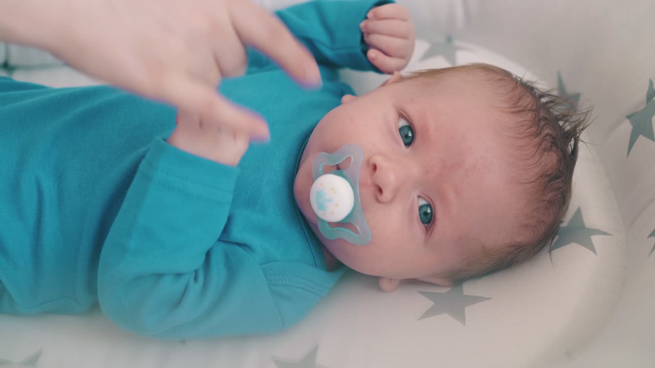 mother gives dummy to crying little baby in cocoon in room