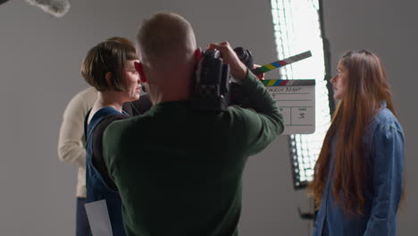 female production assistant uses clapperboard as actors shoot movie or video in studio with film crew and director 3