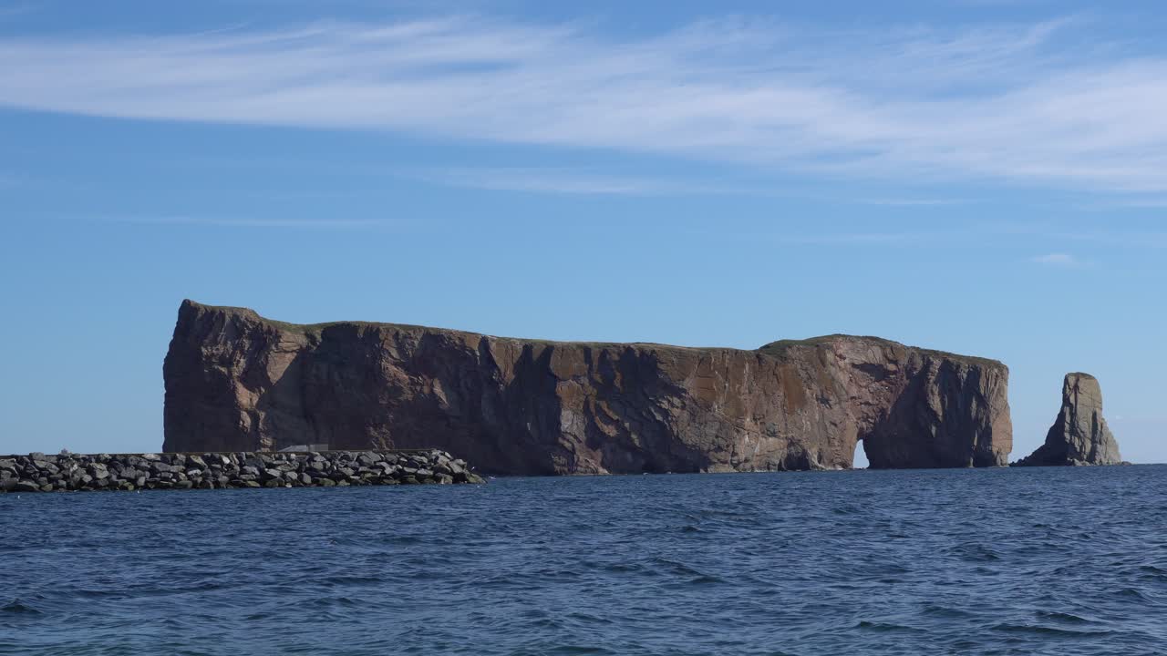You can see the Perce Rock under a beautiful blue sky with clouds. The wind pushes the water directly right away on the shore.