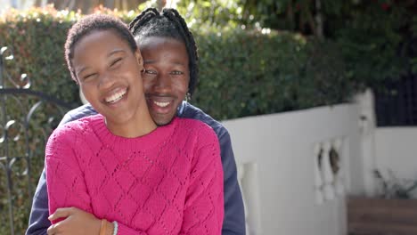 portrait of happy african american couple embracing with copy space in sunny garden, slow motion