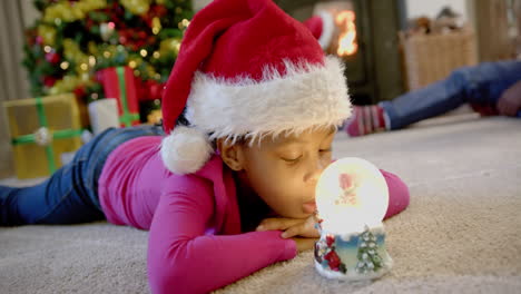 hija afroamericana con sombrero de navidad con globo de nieve brillante, padres detrás, cámara lenta