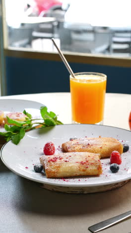 traditional ukrainian nalysnyky with forest fruits and powdered sugar are served on a white plate with a glass of fresh orange juice for a healthy breakfast