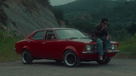 man sitting on vintage red car in the mountains