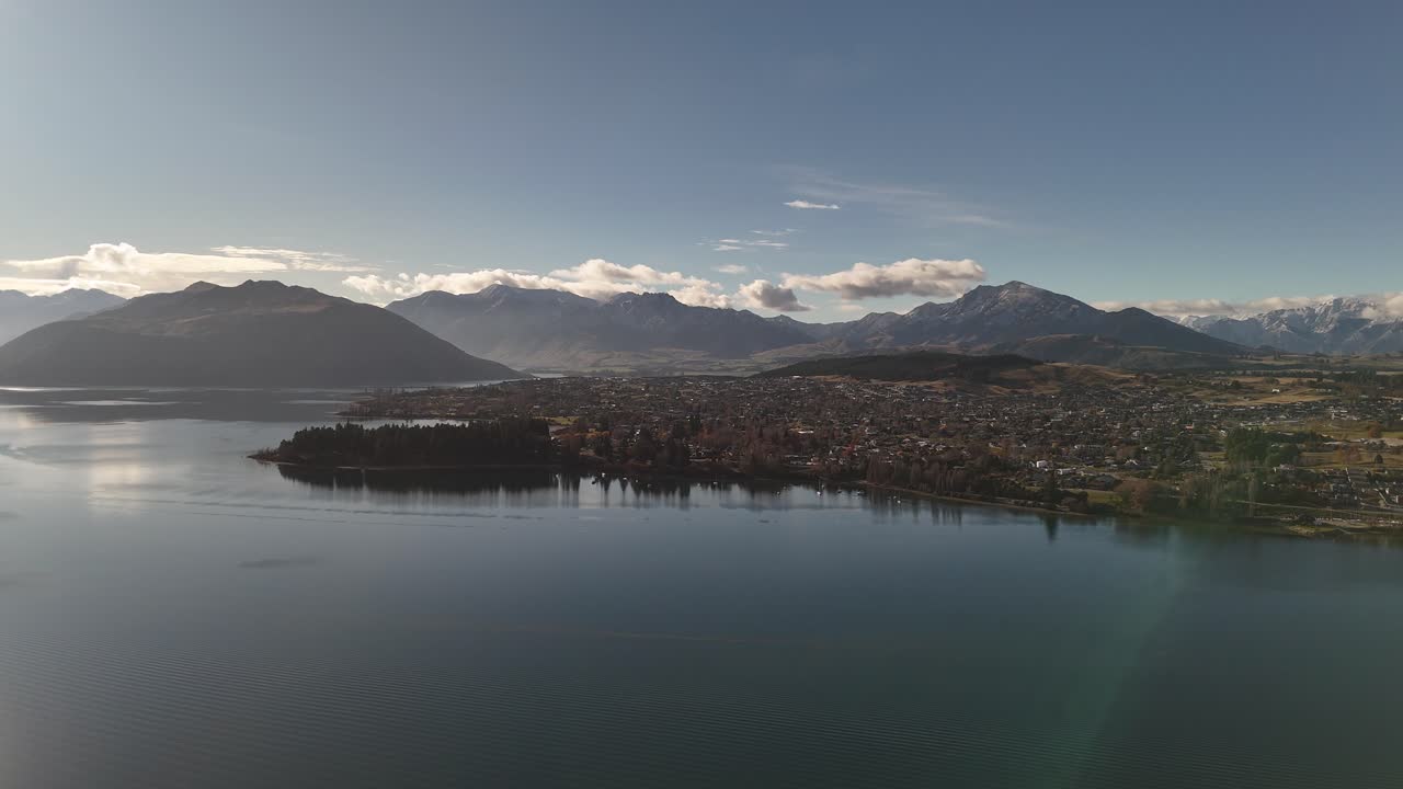Scenic aerial over Lake Wanaka at sunset, showing town and Southern Alps mountain range in background, South Island, New Zealand
