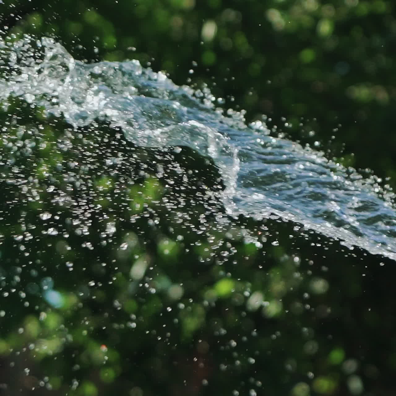 A man with a yellow hose in his hands directs a stream of water directly and higher regulating the process of watering plants in the yard. Close-up.