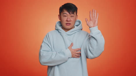 asian man raising hand to take oath, promising to be honest and to tell truth, keeping hand on chest