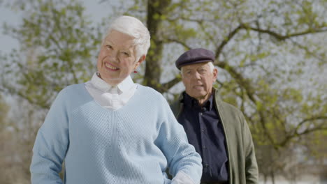 retrato de una anciana mirando a la cámara y sonriendo mientras su marido está detrás en un soleado día de otoño