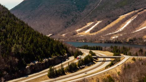 Drone-Aerial-hyper-lapse-time-lapse-of-traffic-on-interstate-with-ski-mountain-and-alpine-lake-in-the-spring-HD-30p