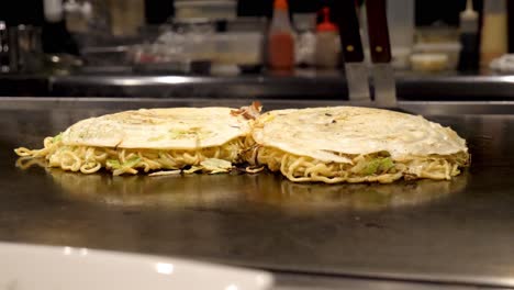 A-Japanese-chef-cooks-a-traditional-Okonomiyaki-savory-pancake-on-a-tepanyaki-grill-in-Kyoto,-Japan