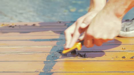 Scraping-off-mastic-sealant-on-wooden-boat-cabin-roof-planks