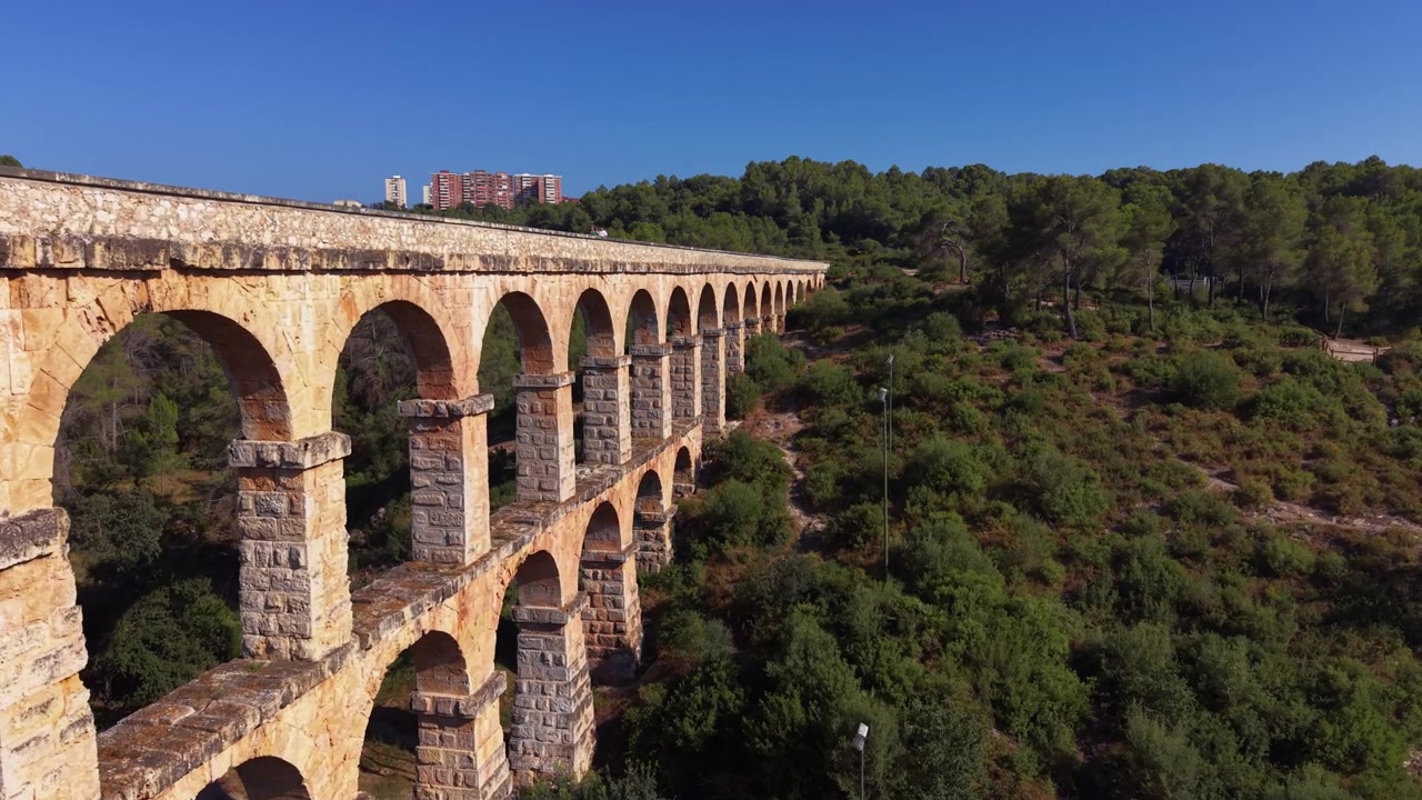 Acquedotto di Les Ferreres a Tarragona, Spagna, un antico acquedotto romano in pietra con arcate a doppio ordine che si erge sopra una lussureggiante foresta verde sotto un cielo azzurro e limpido.