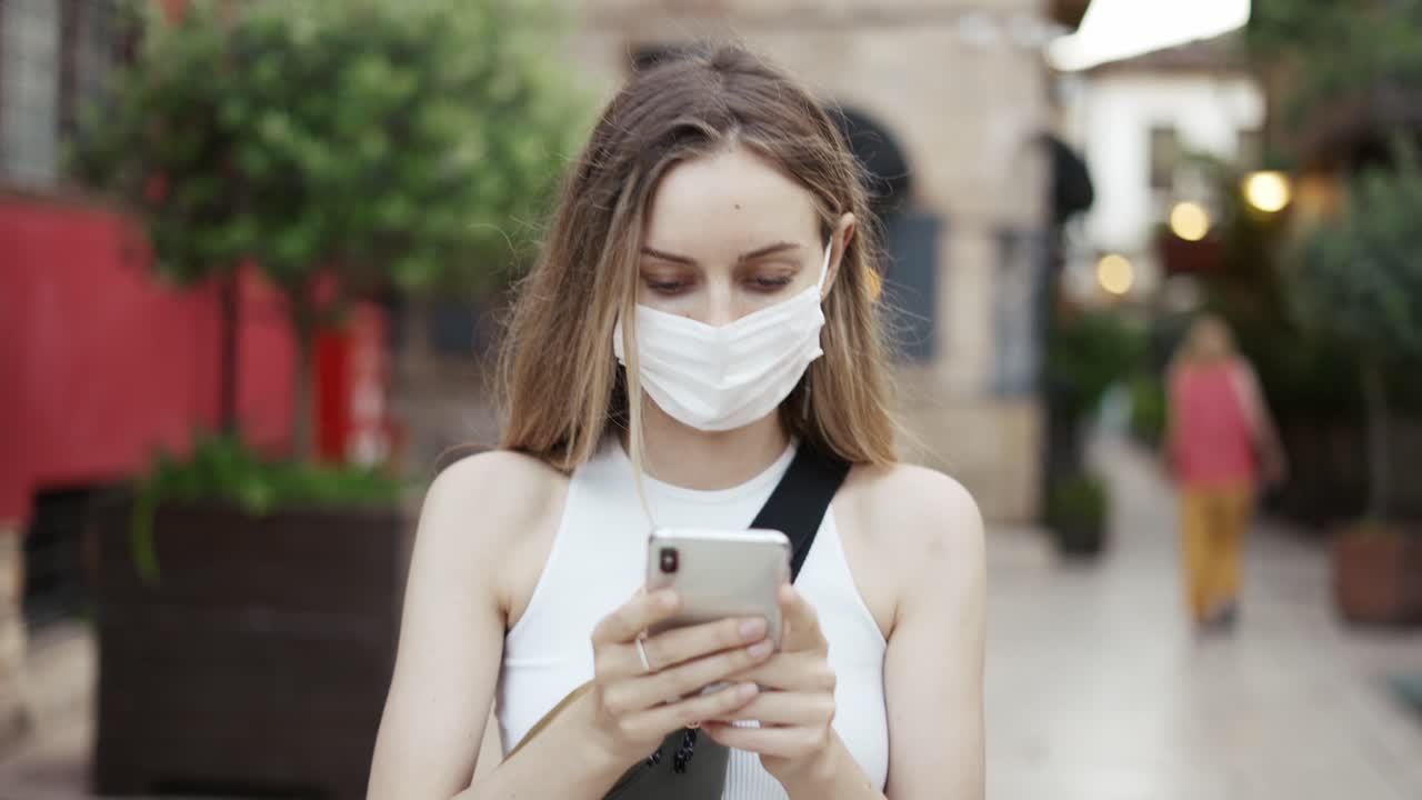 hermosa mujer rubia usando un móvil al aire libre usando una máscara