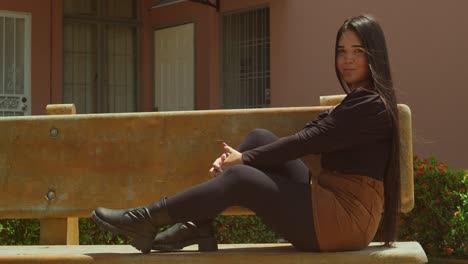 young woman sits on a bench in high heels and mini skirt at a park