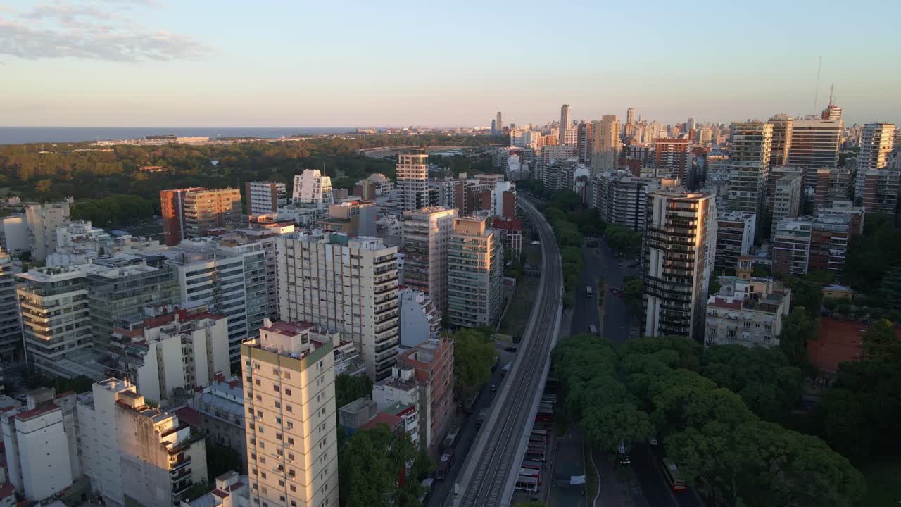 vía aérea a la izquierda de la estación de tren del barrio de belgrano y parques rodeados de edificios con el río de la plata al fondo