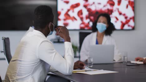 Mixed-race-female-doctor-wearing-mask-giving-presentation-in-meeting-room