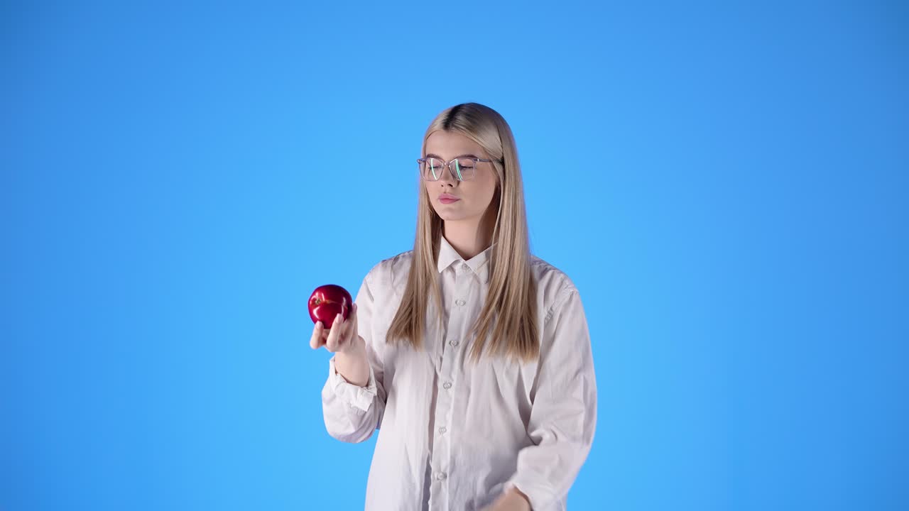joven caucásica juega con una manzana con gafas inteligentes profesor mira morder la fruta