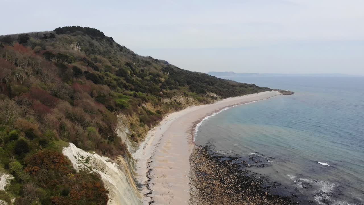 Aerial view capturing the serene coastline of Seaton undercliffs near Lyme Regis, showcasing lush greenery and calm ocean waves. Circle Dolly Shot