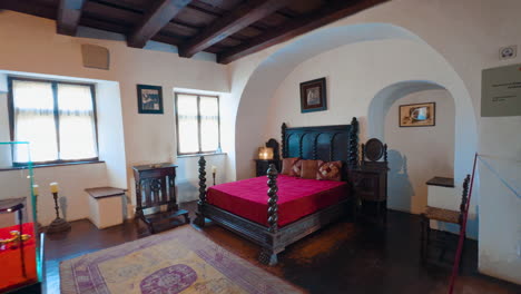 interior of the medieval bran castle in brasov, romania. approaching big wooden bed with red cover on.