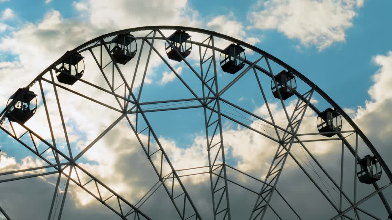 Silhouette of ferris wheel rotating against blue sky with dramatic clouds